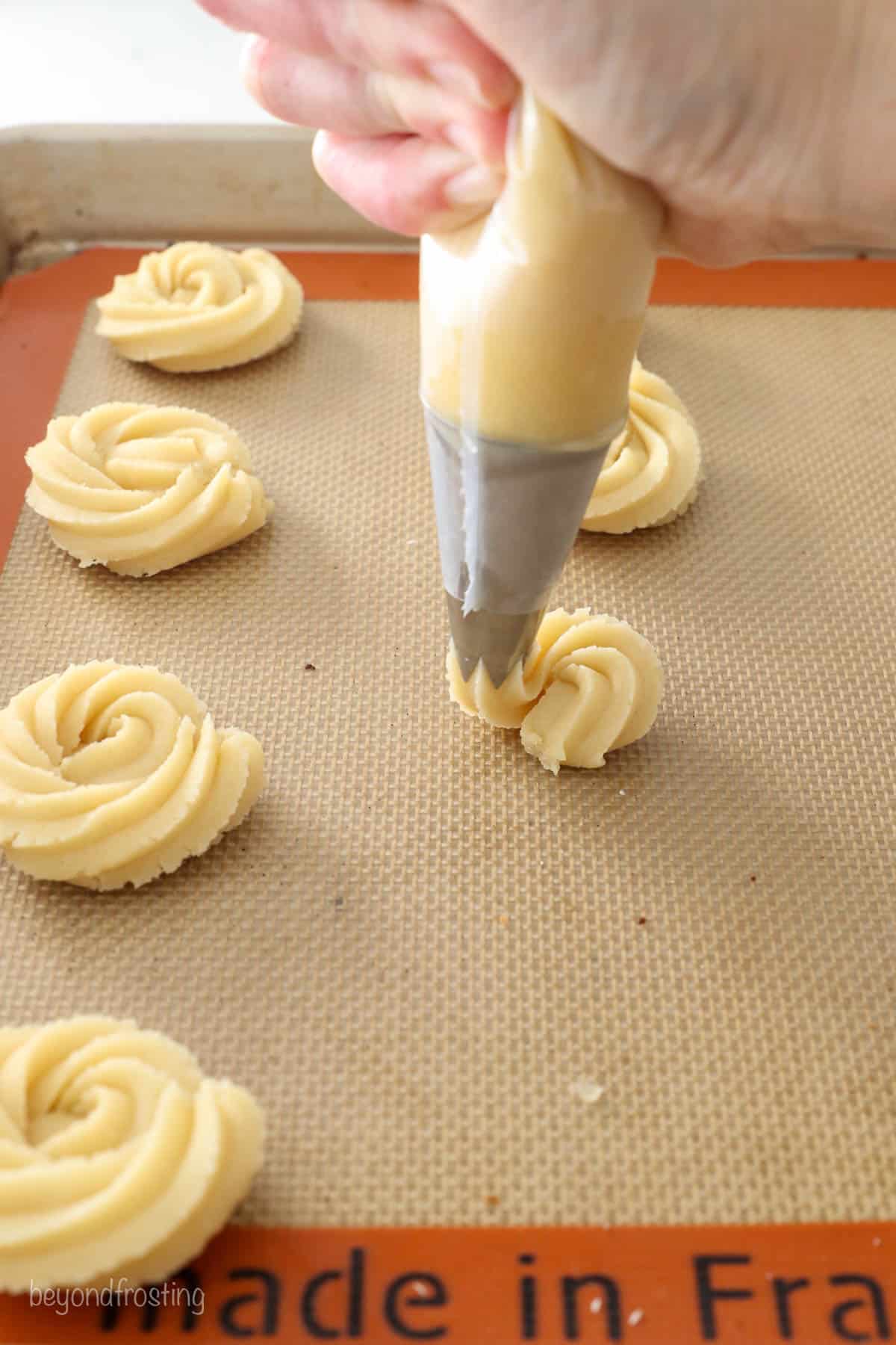 Butter cookie dough being piped onto a silicone-lined baking sheet with a wide open star piping tip