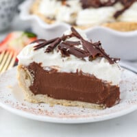 A close up of a sliced chocolate pie on a white plate dusted with cocoa powder