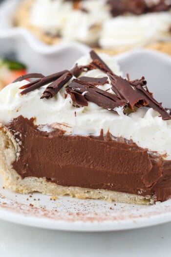 A close up of a sliced chocolate pie on a white plate dusted with cocoa powder