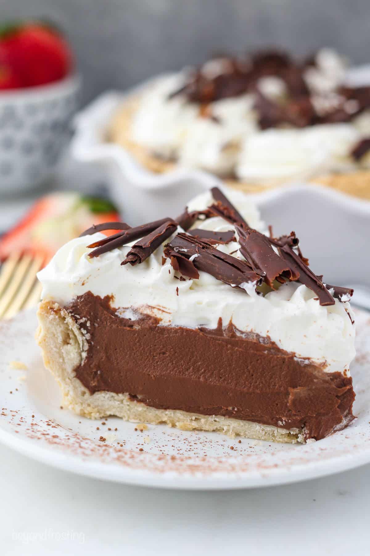 A close up image of a slice of chocolate pie with whipped cream and chocolate shavings