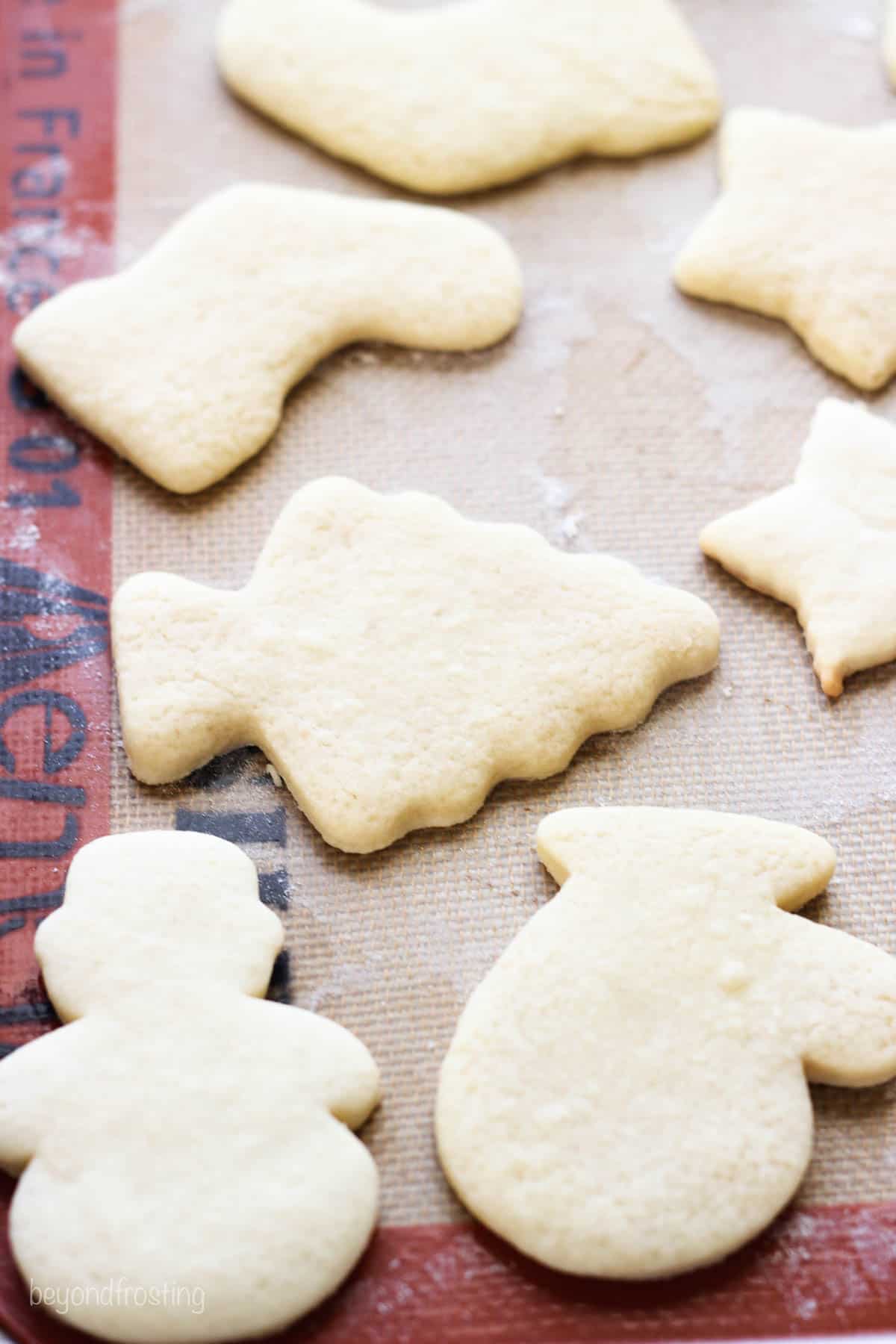 Baked cut out cookies on a silicone lined tray, Christmas tree, Snowman, Stockings and gloves