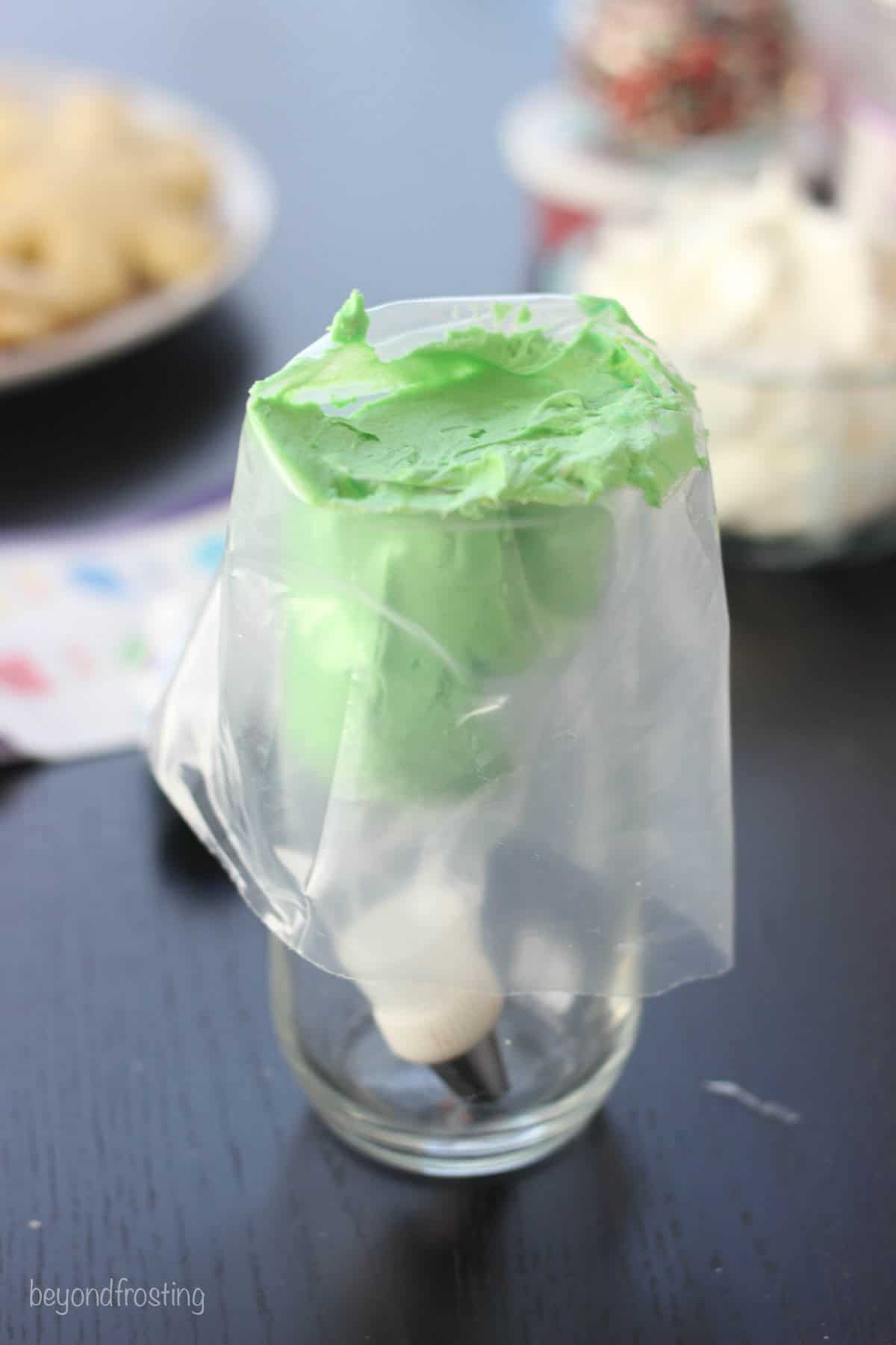 a glass with a piping bag pulled over the side and filled with buttercream