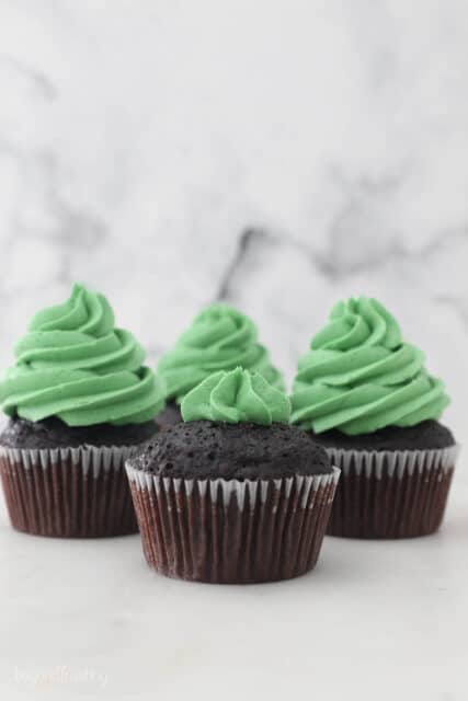 A piping bag filled with green frosting, piping a chocolate cupcake