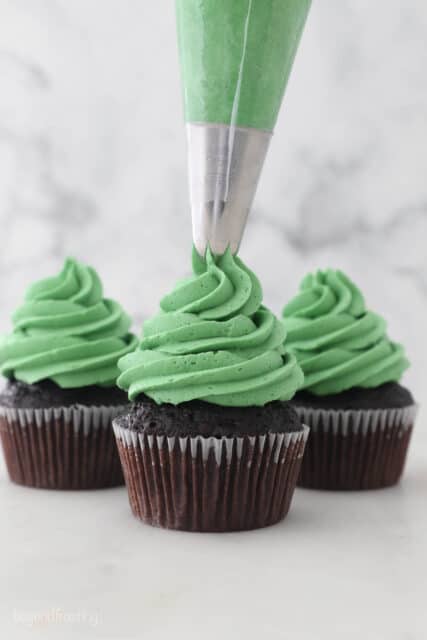 A piping bag filled with green frosting, piping a cupcake