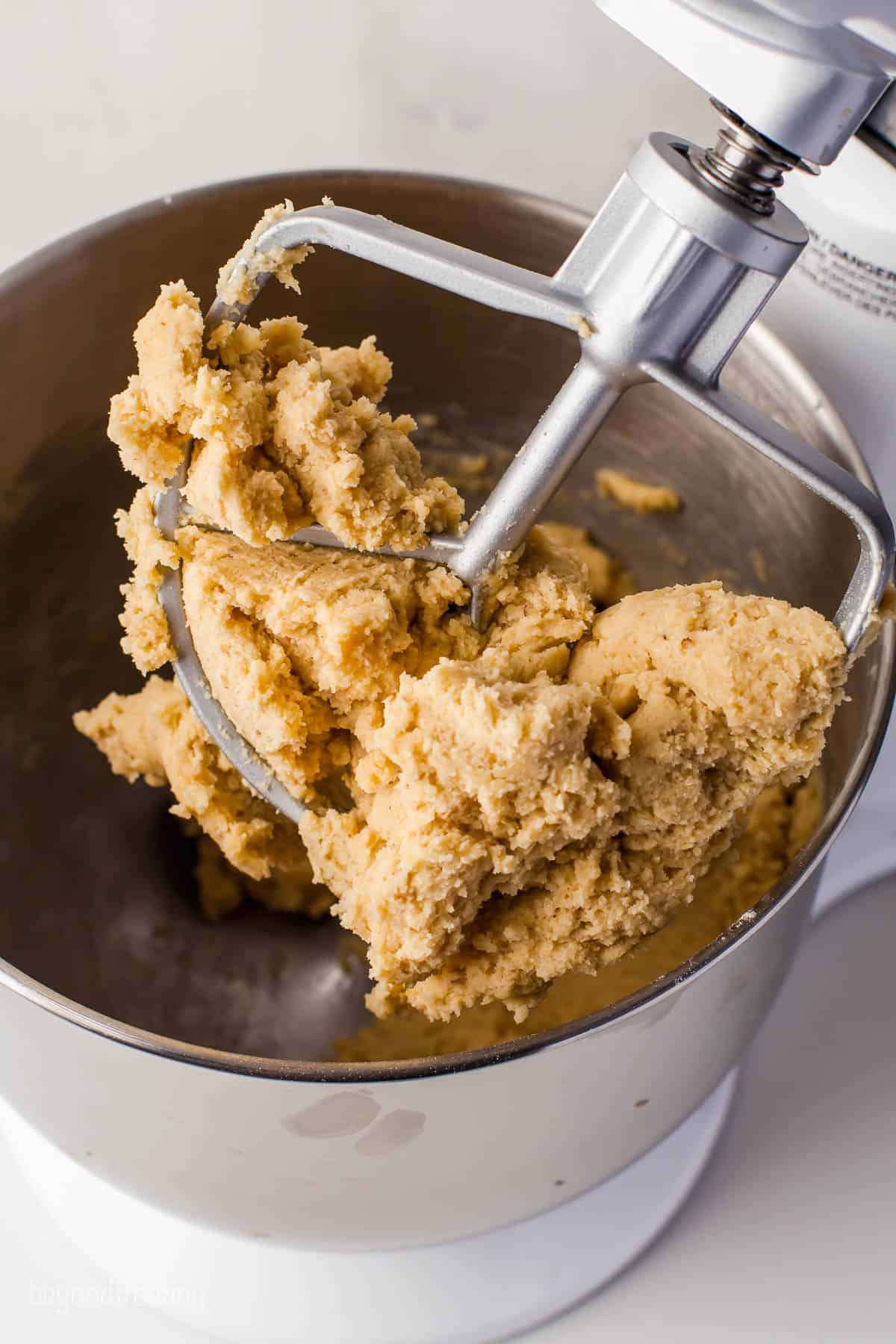 A stand mixer holding up a large amount of cookie dough over a metal mixing bowl