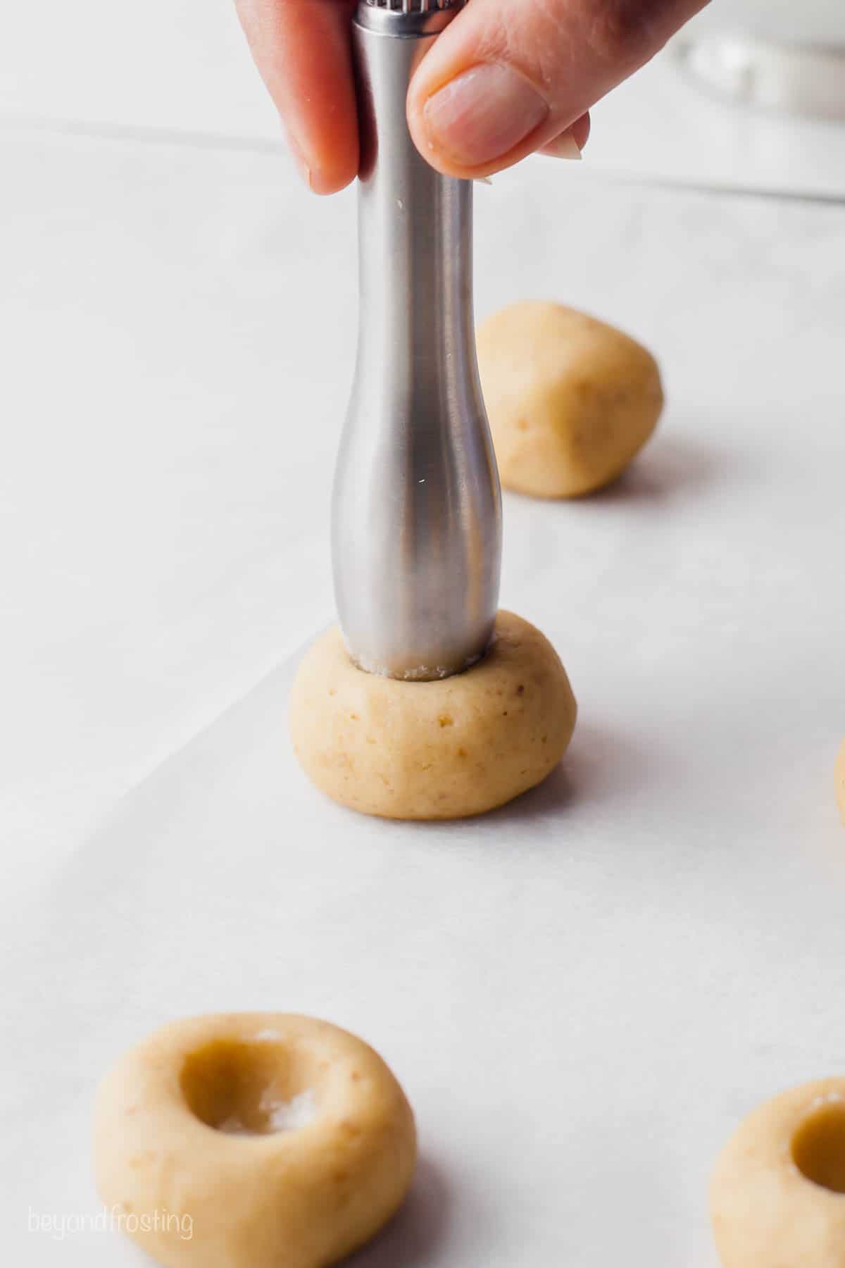 A metal cooking tool being poked into a ball of cookie dough to form a well for the filling