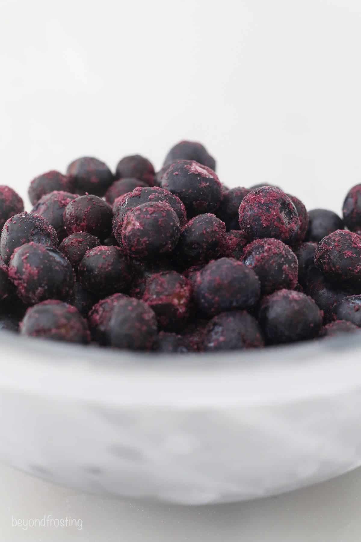 a close up of frozen blueberries in a glass mixing bowl