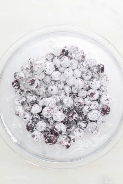 a glass mixing bowl with blueberries that are coated with corn starch
