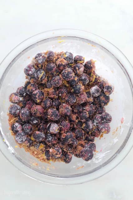 a glass mixing bowl with blueberries tossed with brown sugar and lemon zest