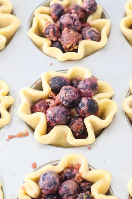 a close up of unbaked blueberry pies in a muffin pan
