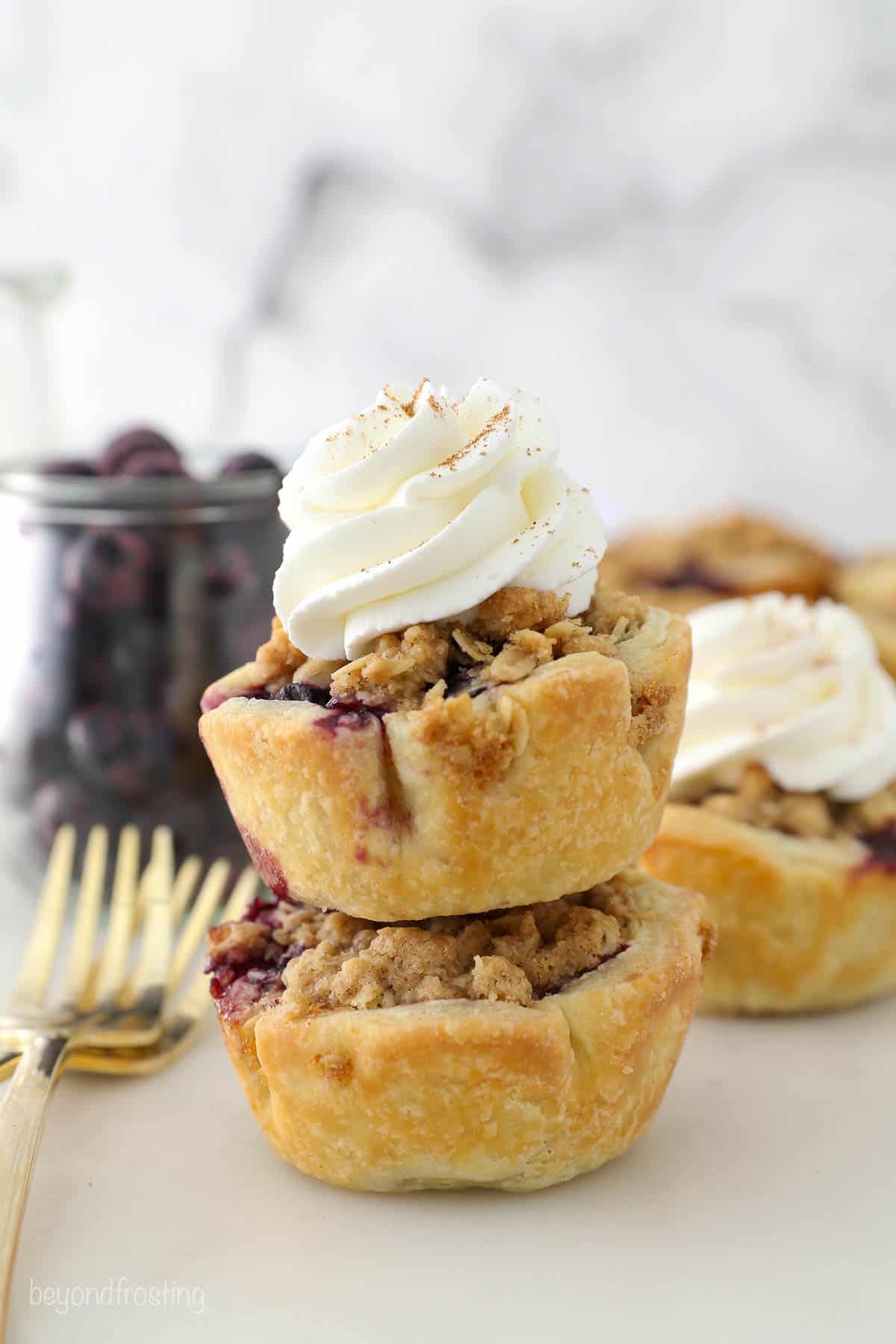 Two mini blueberry pies stacked, with gold forks next to them