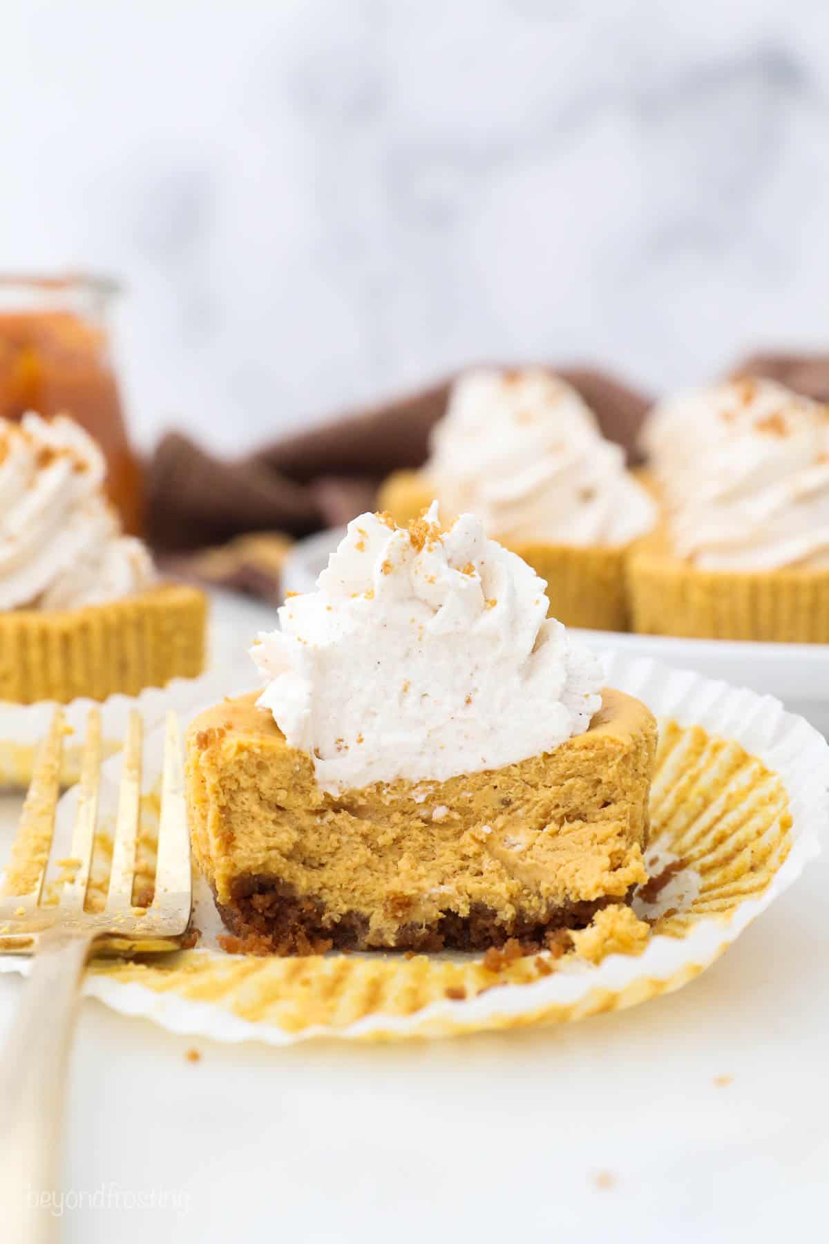 Half eaten mini pumpkin cheesecake with the wrapper folded down and a gold fork laying next to it