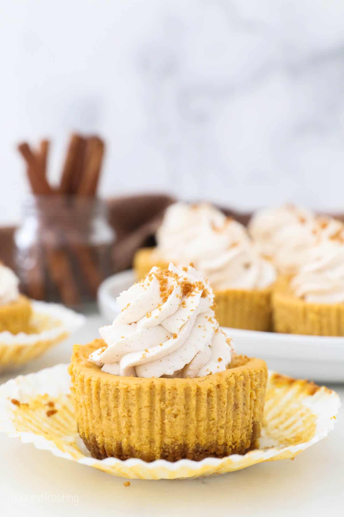 Unwrapped mini pumpkin cheesecake with whipped cream and cinnamon sticks in the background