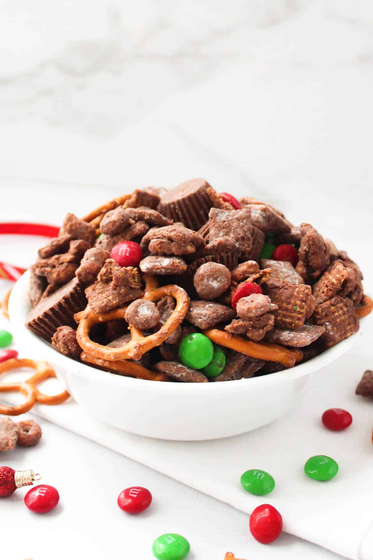 reindeer chow snack mix in a white bowl surrounded with green and red M&Ms