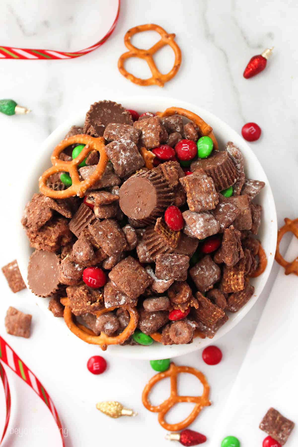 a white bowl fill with Christmas snack mix like pretzels, Reese's peanut butter cups and pretzels
