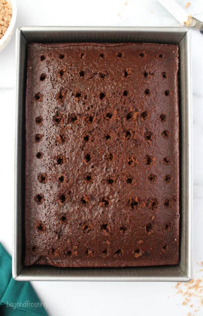 A chocolate cake on a kitchen countertop with holes poked into it