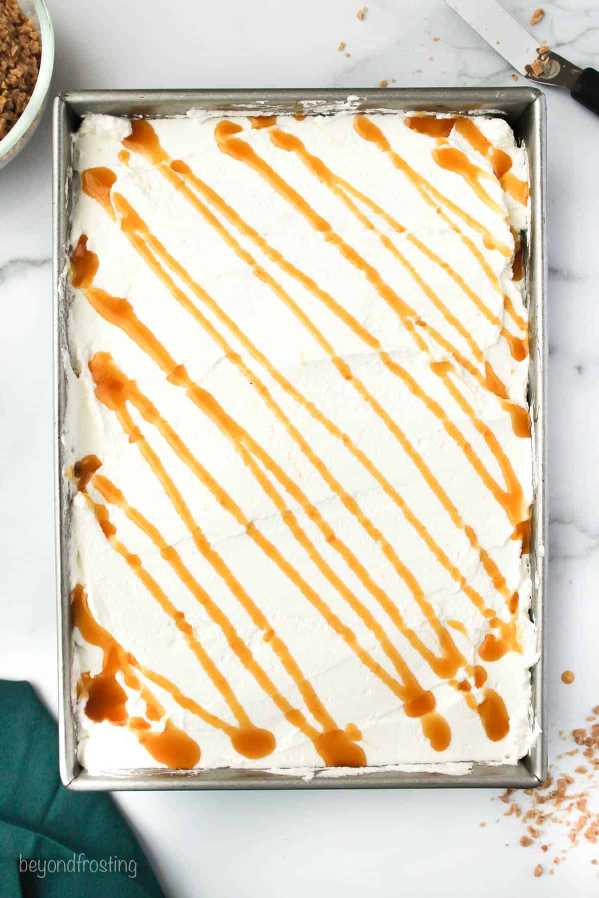 A caramel chocolate cake in a pan frosted with whipped cream and drizzled with extra caramel