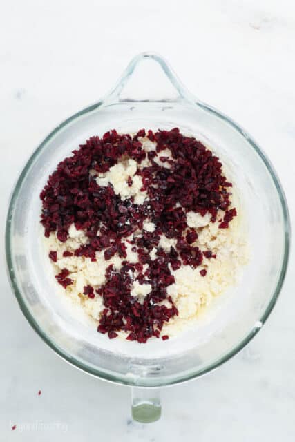 A glass mixing bowl with crumbled butter, sugar and flour and sliced cranberries