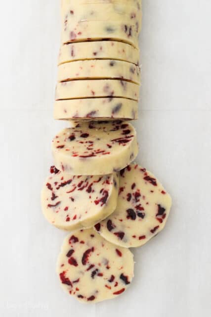 A roll of shortbread dough with cranberries is showing sliced pieces
