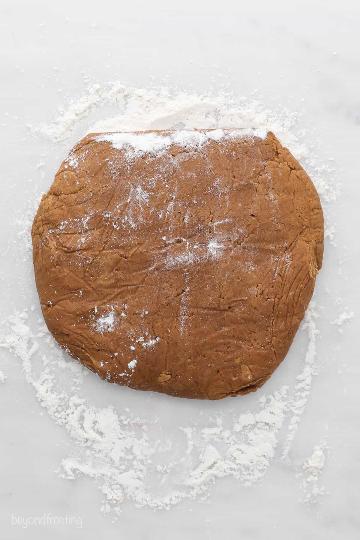 A disc of chilled gingerbread cookie dough on a countertop covered in flour
