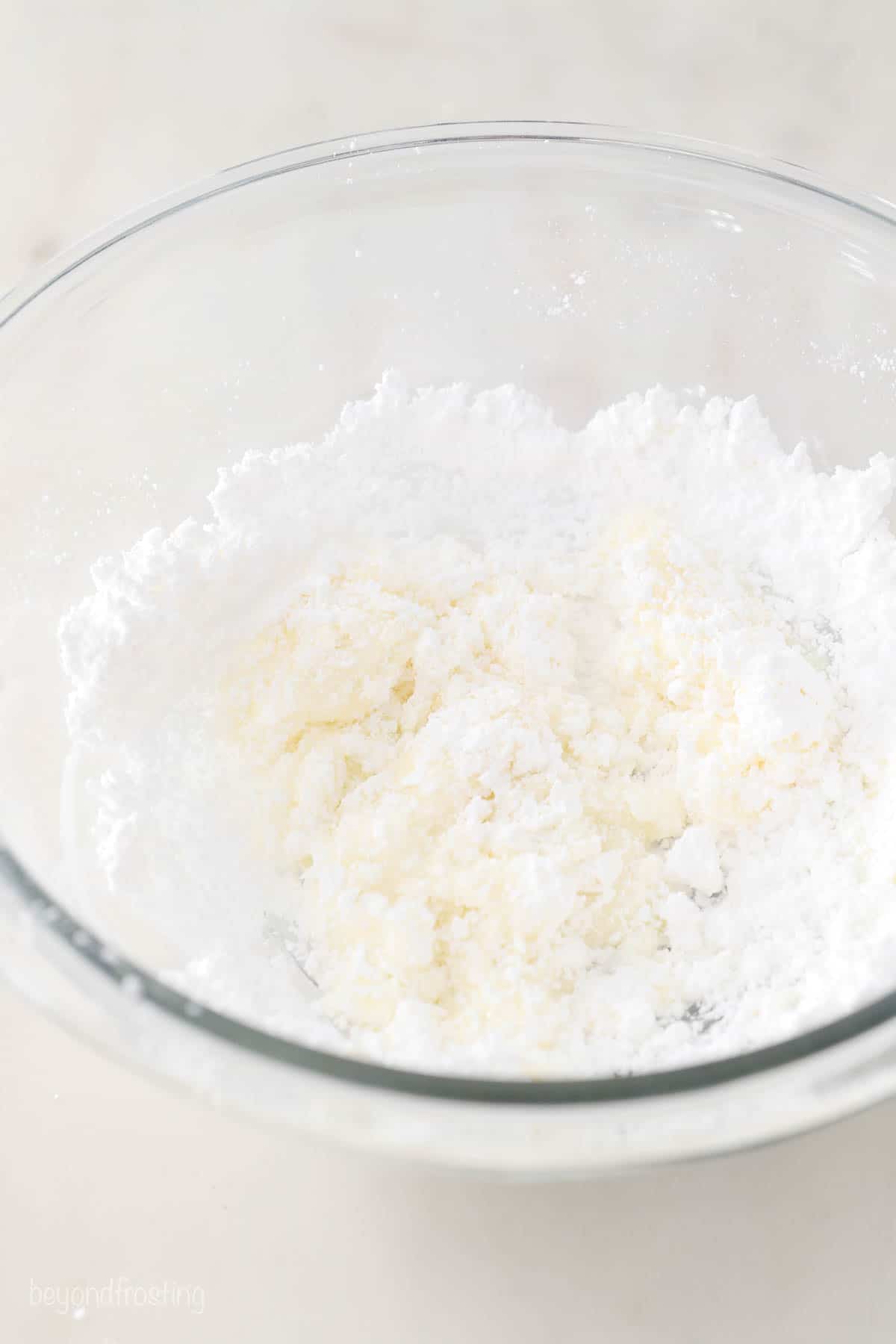 Powdered sugar being combined with milk in a large glass mixing bowl