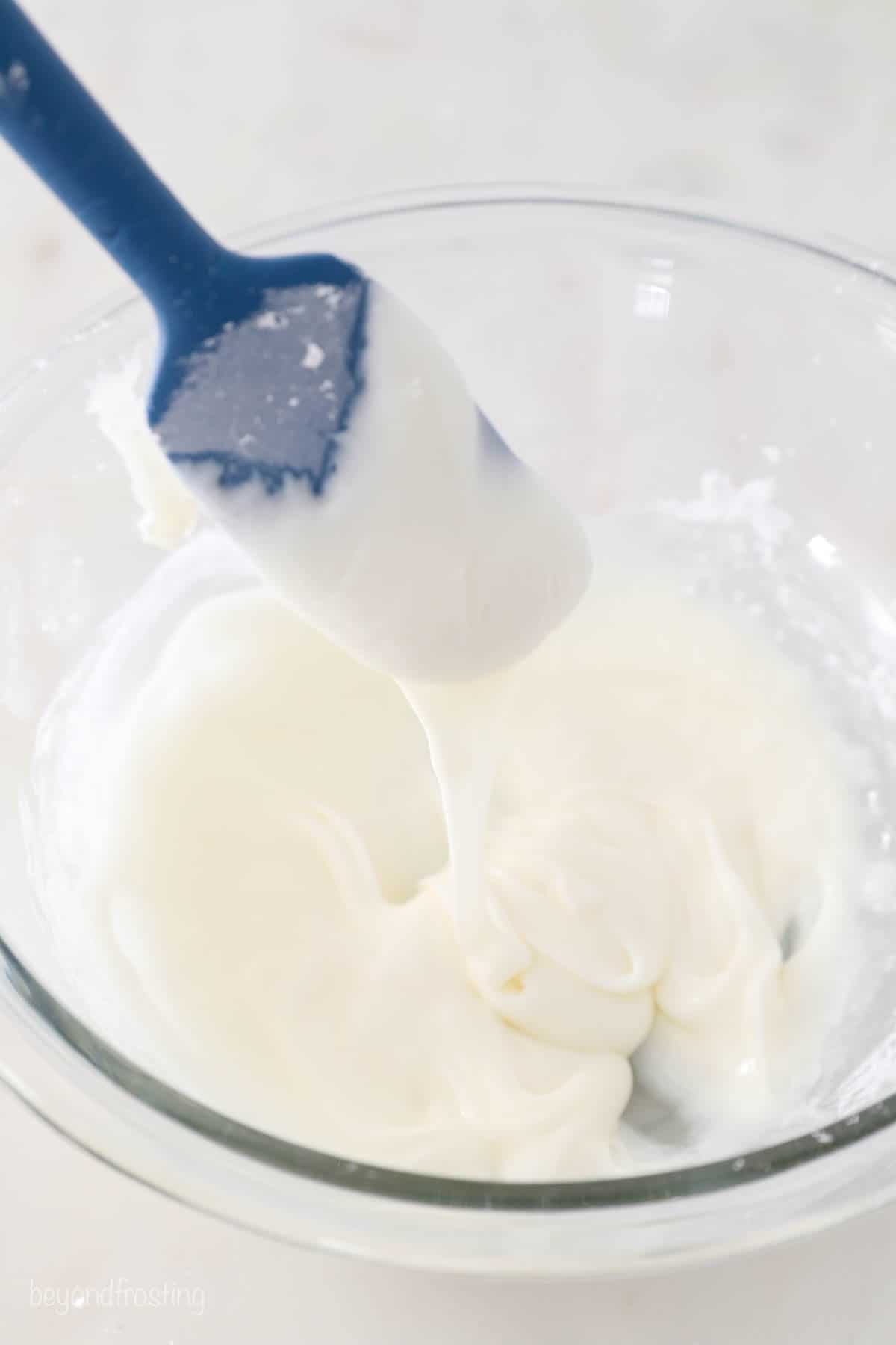 A batch of icing in a large glass bowl with a rubber spatula scooping some out