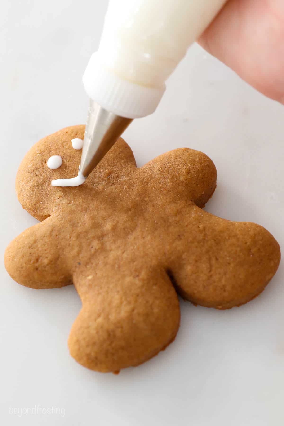 Icing being used to pipe a smiling face onto a homemade gingerbread cookie