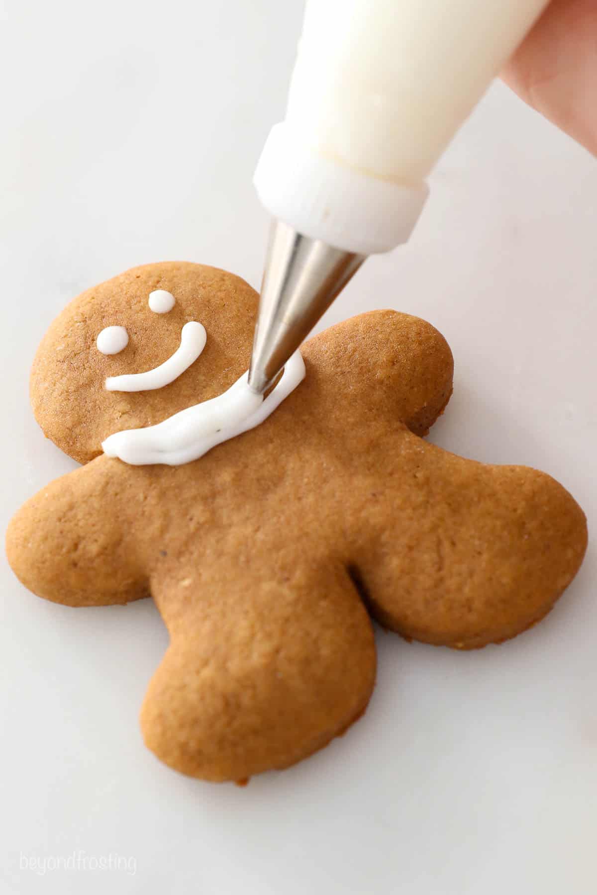 A scarf being piped onto a cooled gingerbread cookie with bright white icing
