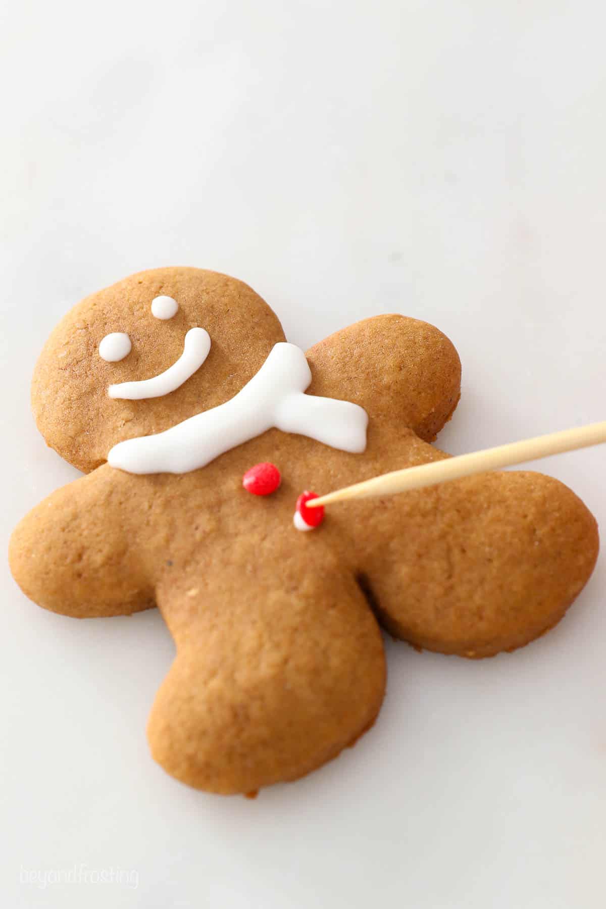 A red sprinkle being added to a soft gingerbread man cookie on top of a dot of icing