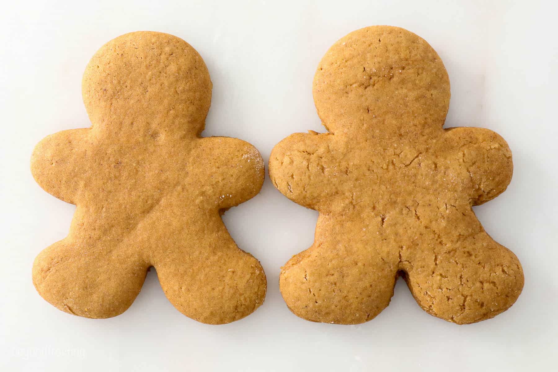 Two gingerbread men cookies laying side by side on a kitchen countertop