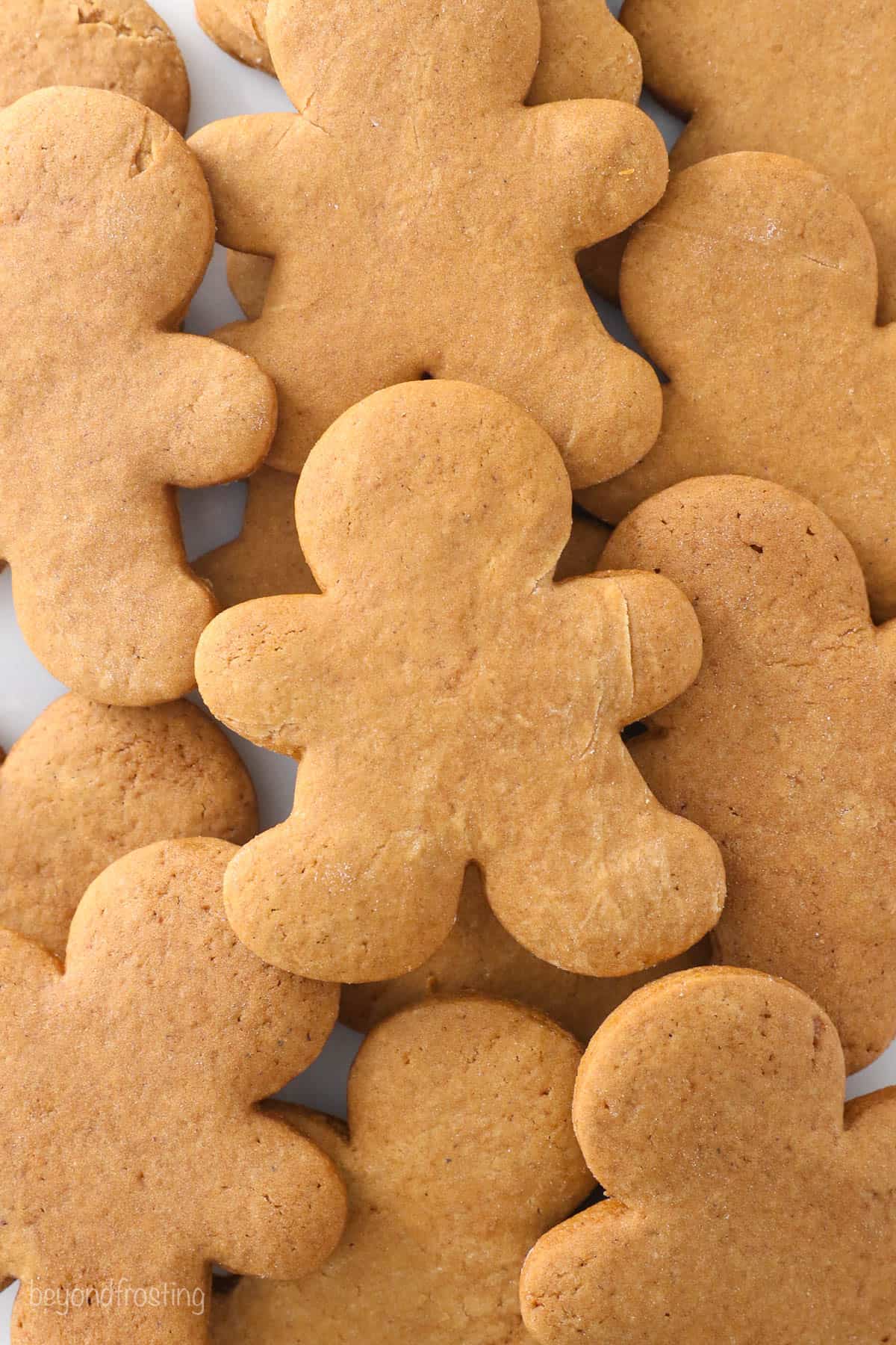 A pile of unfrosted gingerbread man cookies on top of a plain white surface