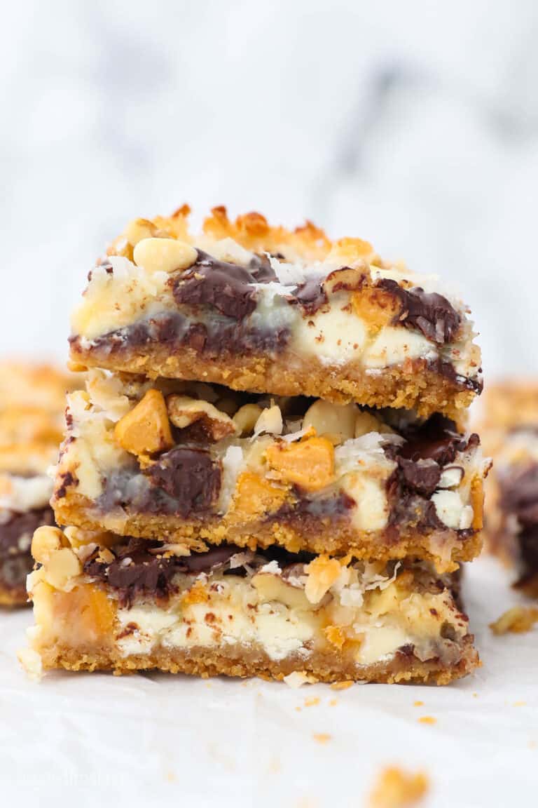 Three seven layer dessert bars stacked on top of one another with more bars in the background