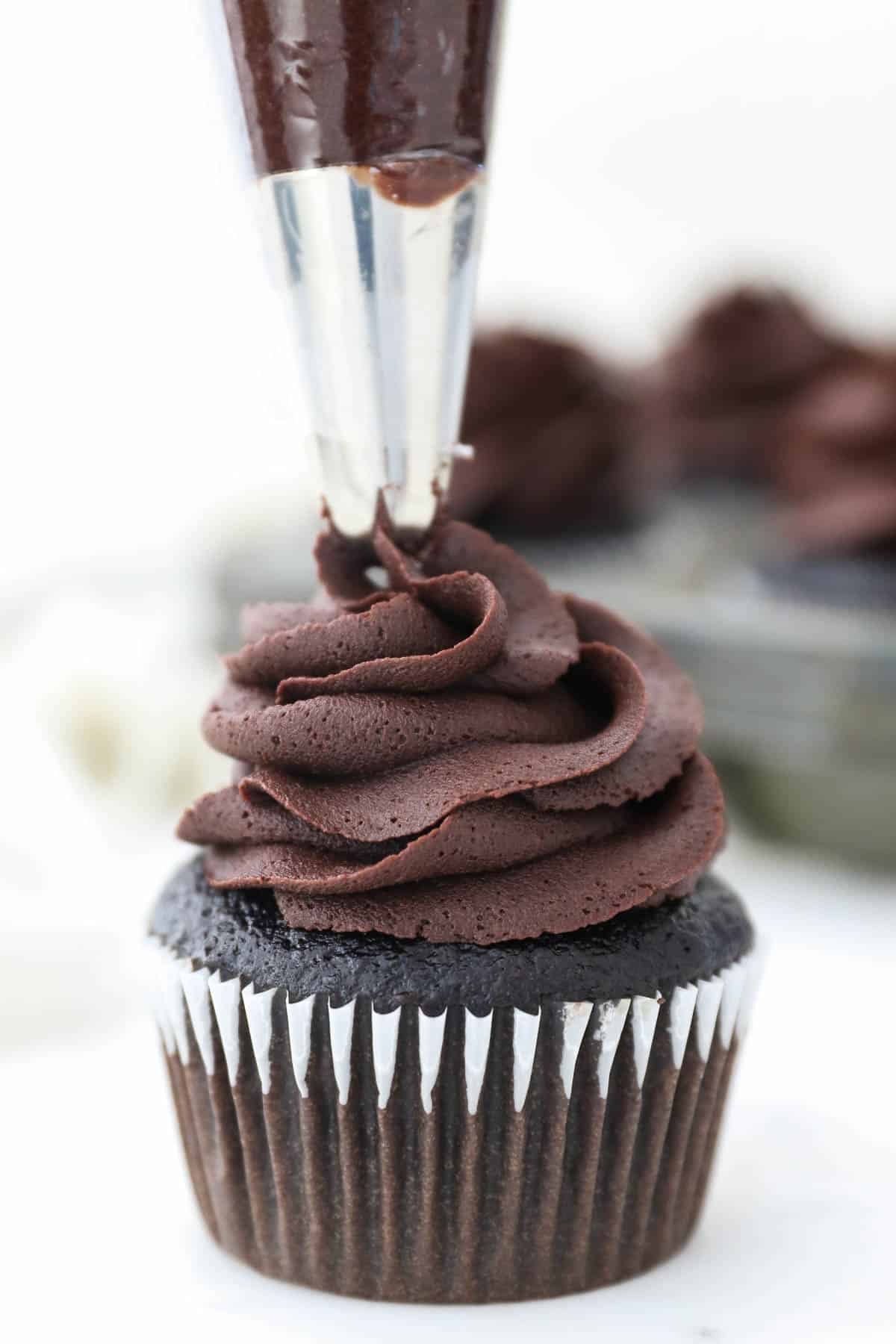 A piping bag with chocolate frosting piping a cupcake