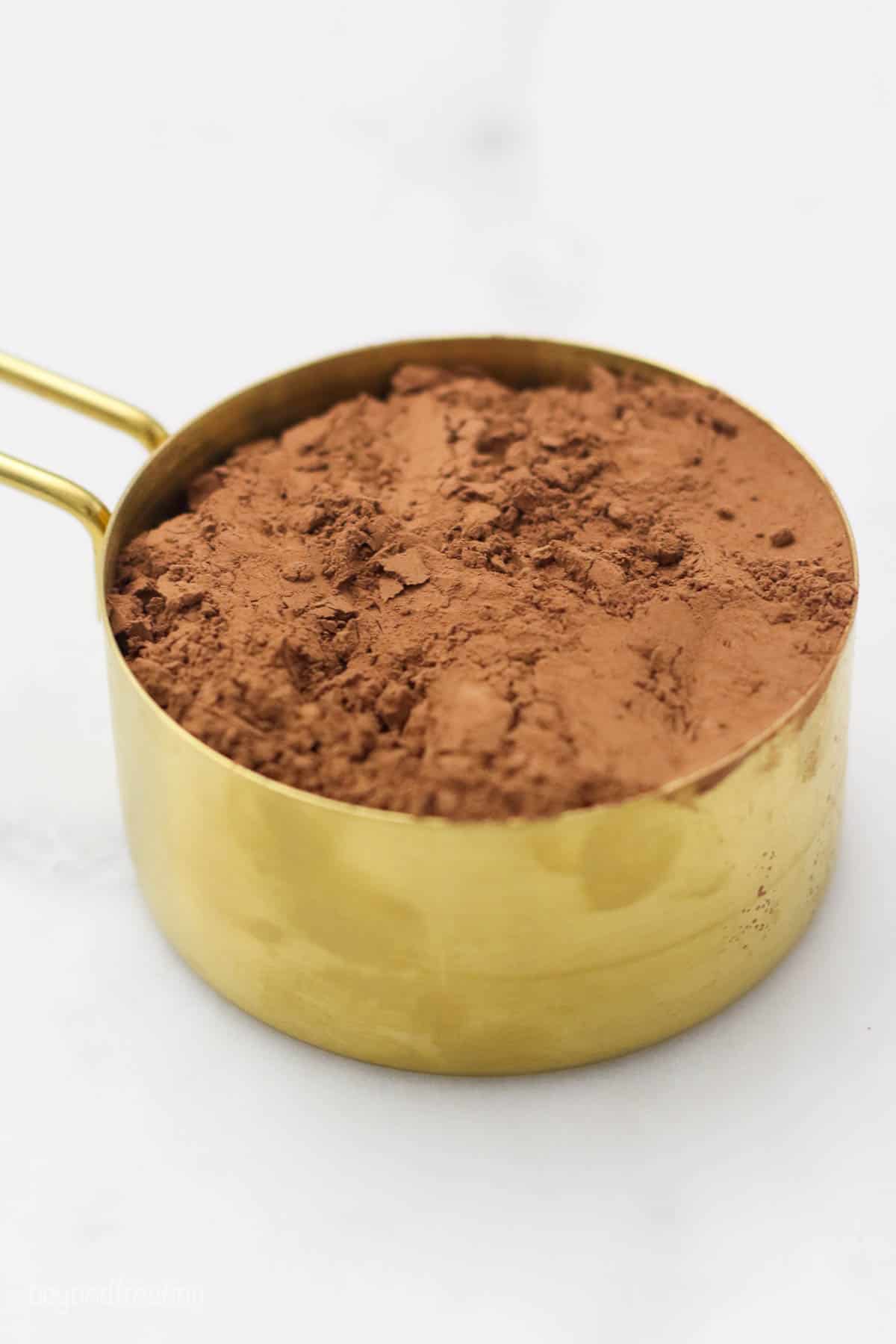 A gold measuring cup filled with cocoa powder