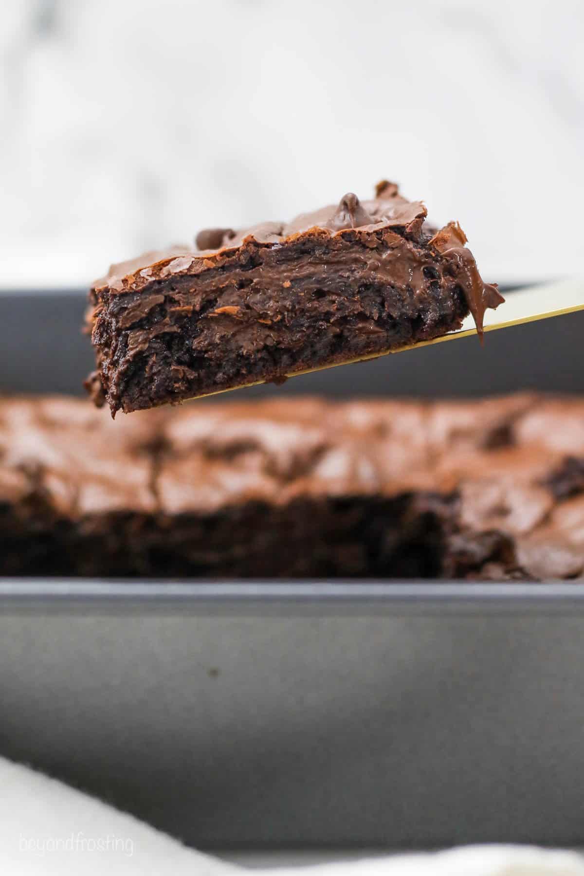 A gold spatula holding a melty fudge brownie over the top of the pan