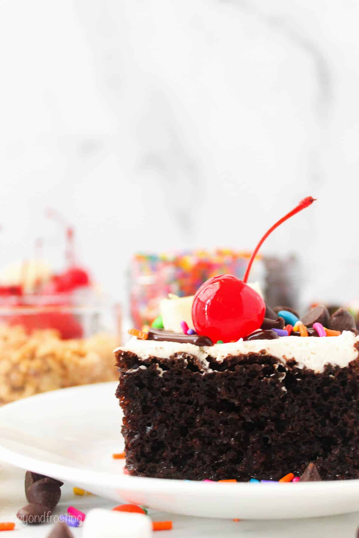 side view of a slice of chocolate poke cake decorated with hot fudge sundae toppings