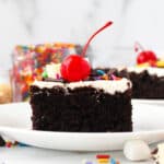 closeup of a slice of hot fudge sundae cake with toppings on a white plate