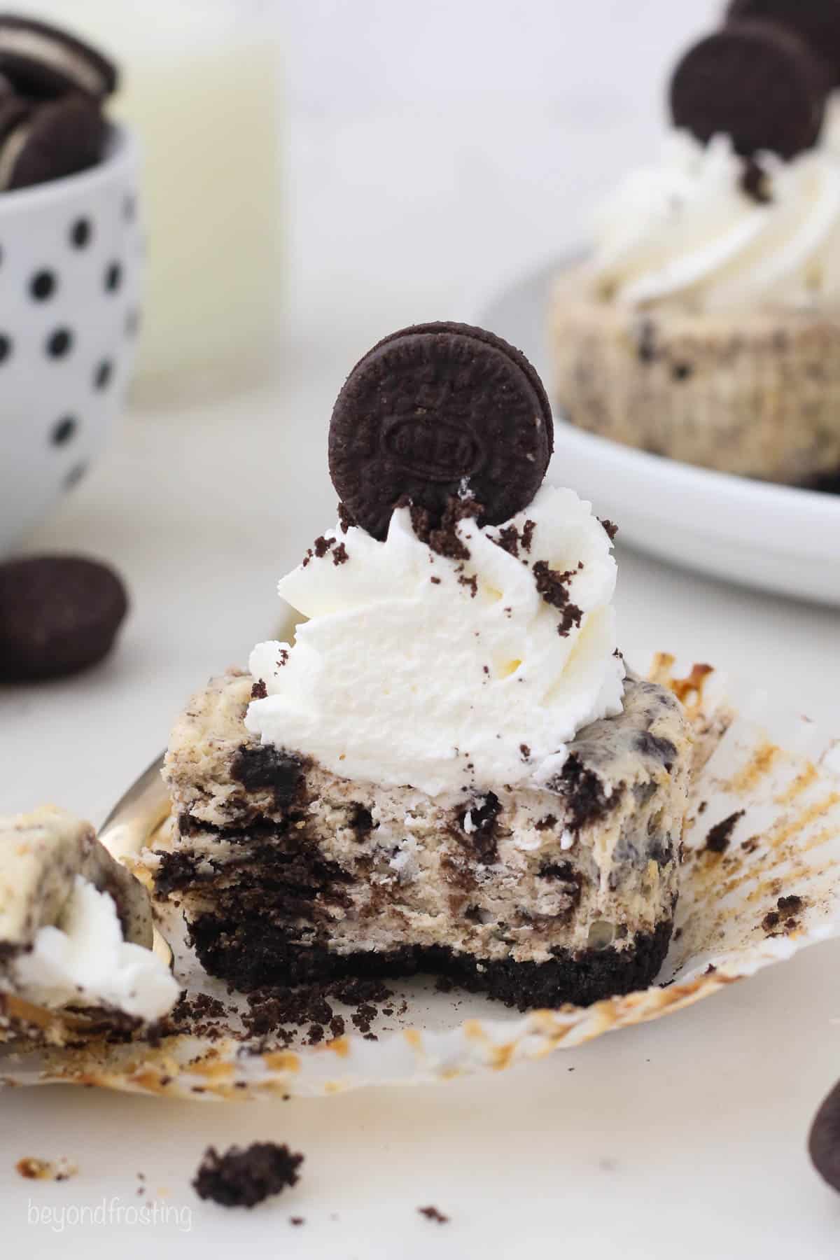 A mini Oreo cheesecake cut in half with a bowl of Oreo cookies behind it