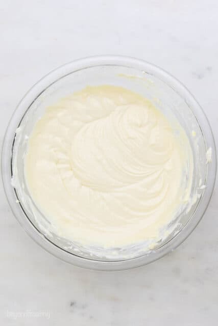 The whipped cream topping in a glass mixing bowl on a marble countertop