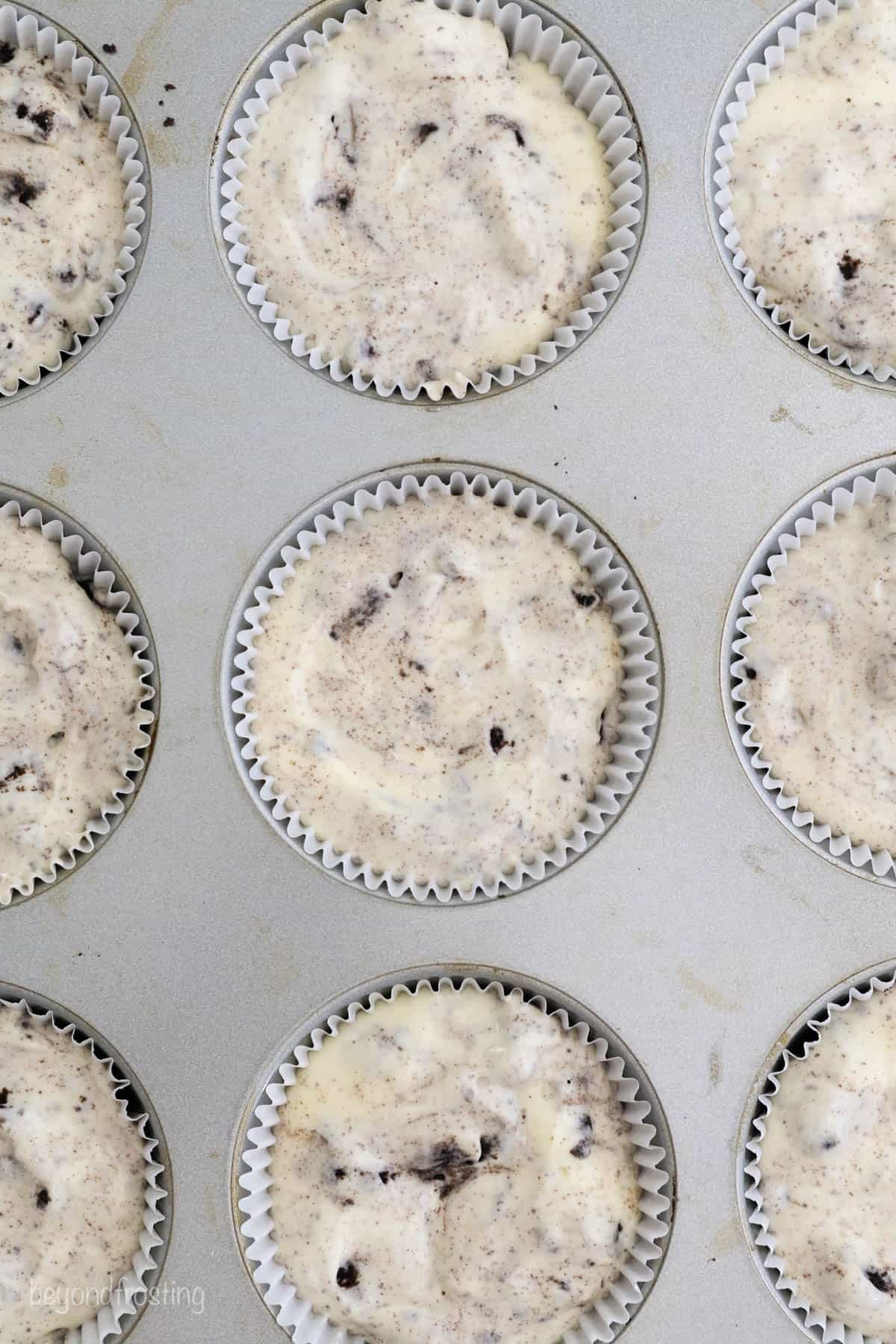 Baking liners in a cupcake pan filled with Oreo crust and cheesecake filling