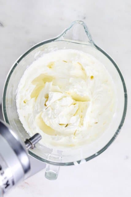 A stand mixer with whipped cream in a glass bowl