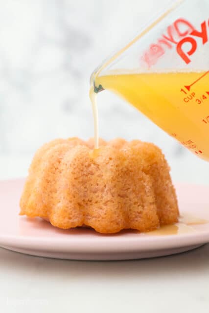 Syrup being poured from a pryex measuring cup over top of a mini bundt cake