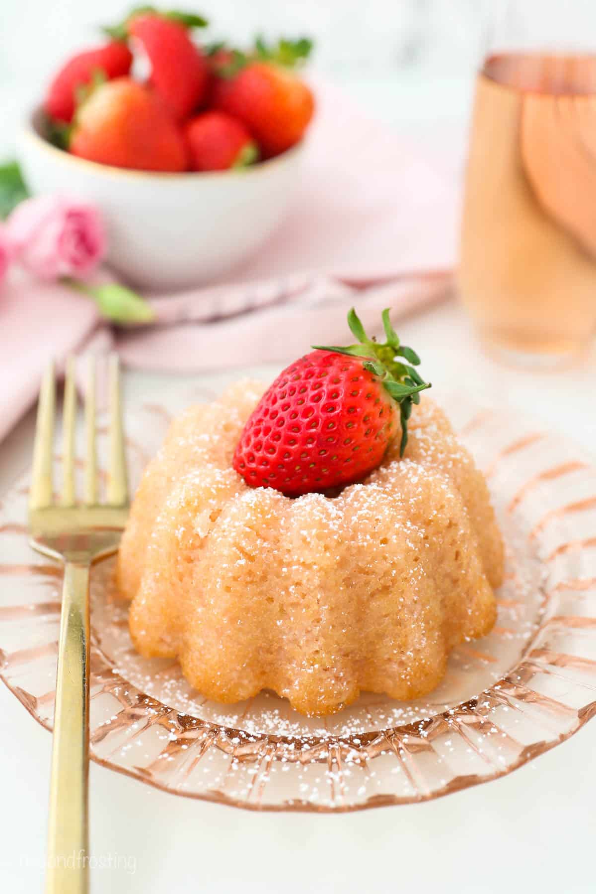 A pink glass glass with a mini bundt cake topped with a strawberry