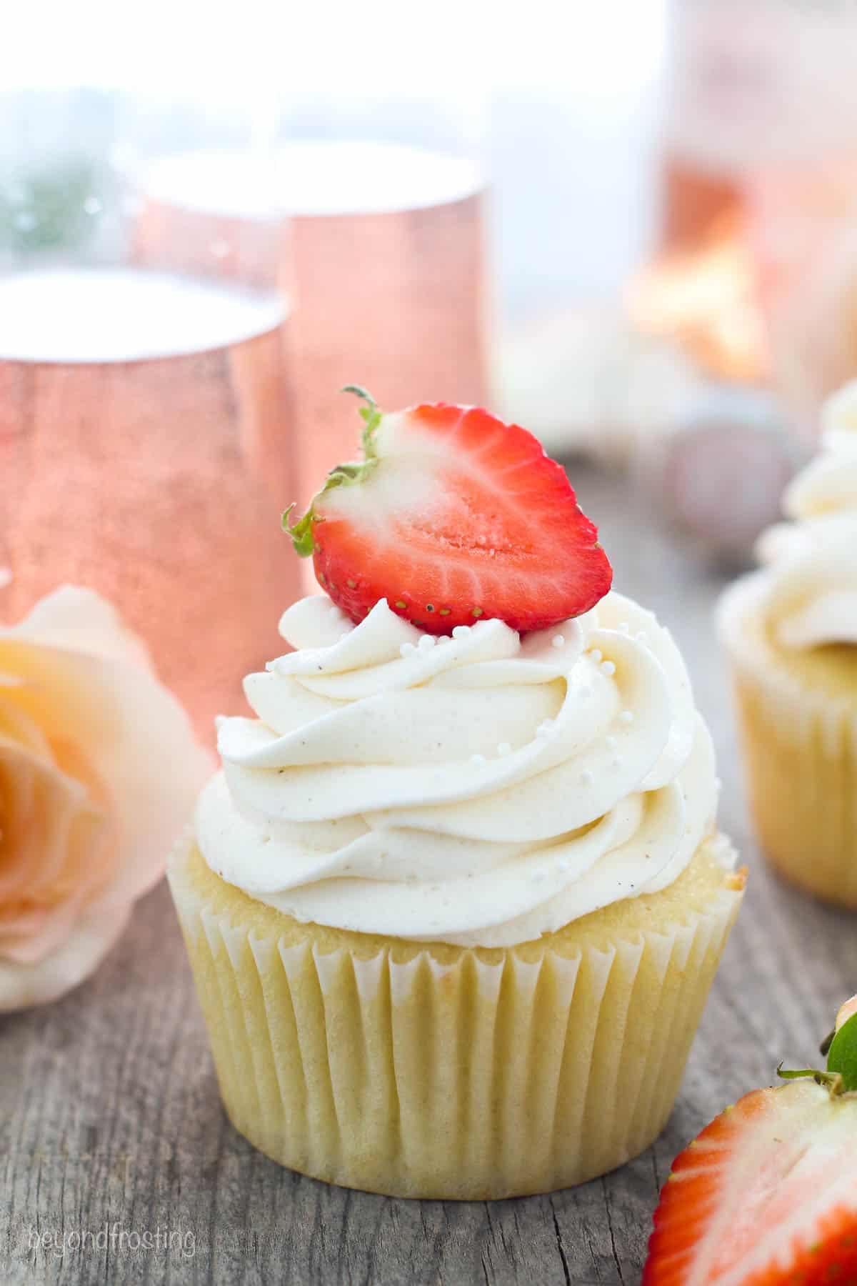 one strawberry rosé cupcake topped with half strawberry with two glasses of rosé in the background