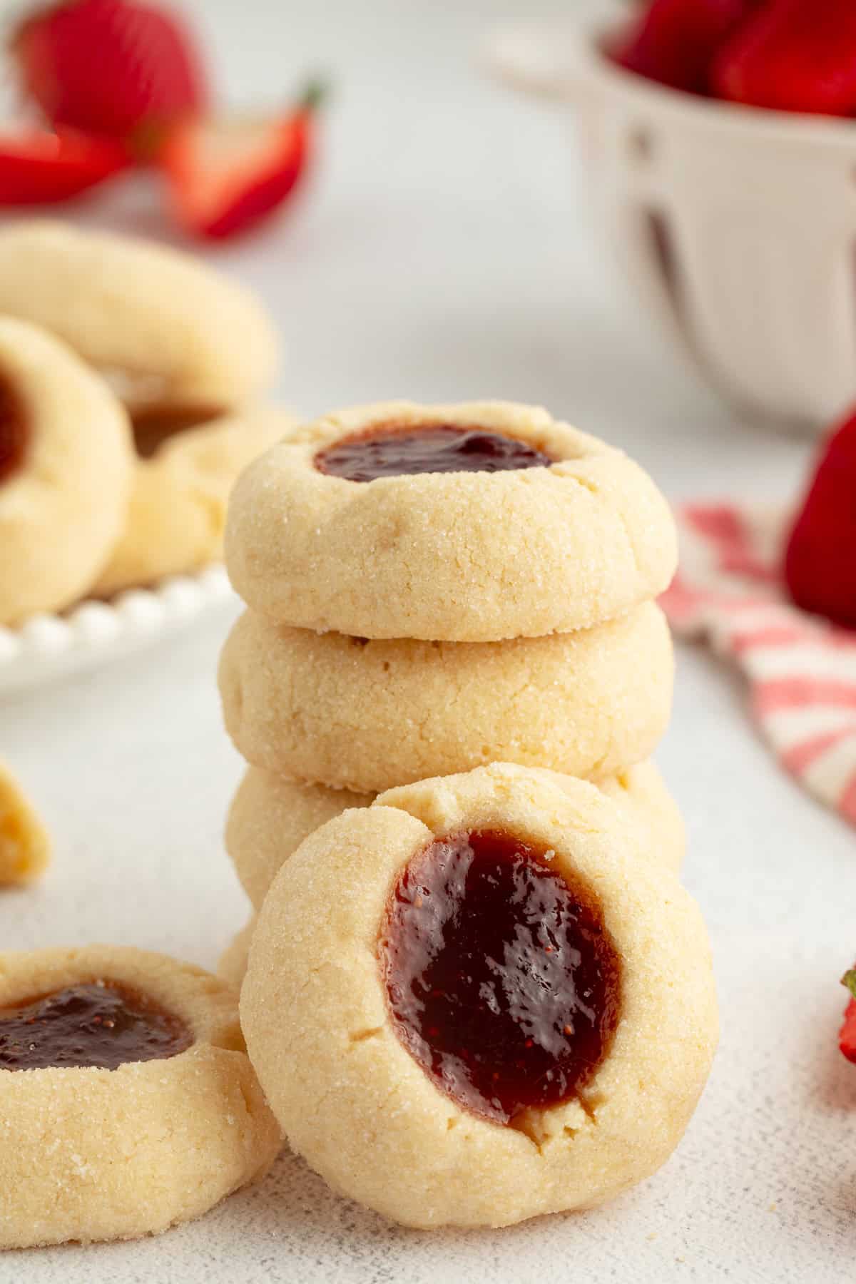 Thumbprint cookies are buttery, melt-in-your-mouth shortbread cookies rolled in sugar, filled with fruit jam, chocolate, caramel, and more. A thumbprint cookie propped up against a stack of cookies.