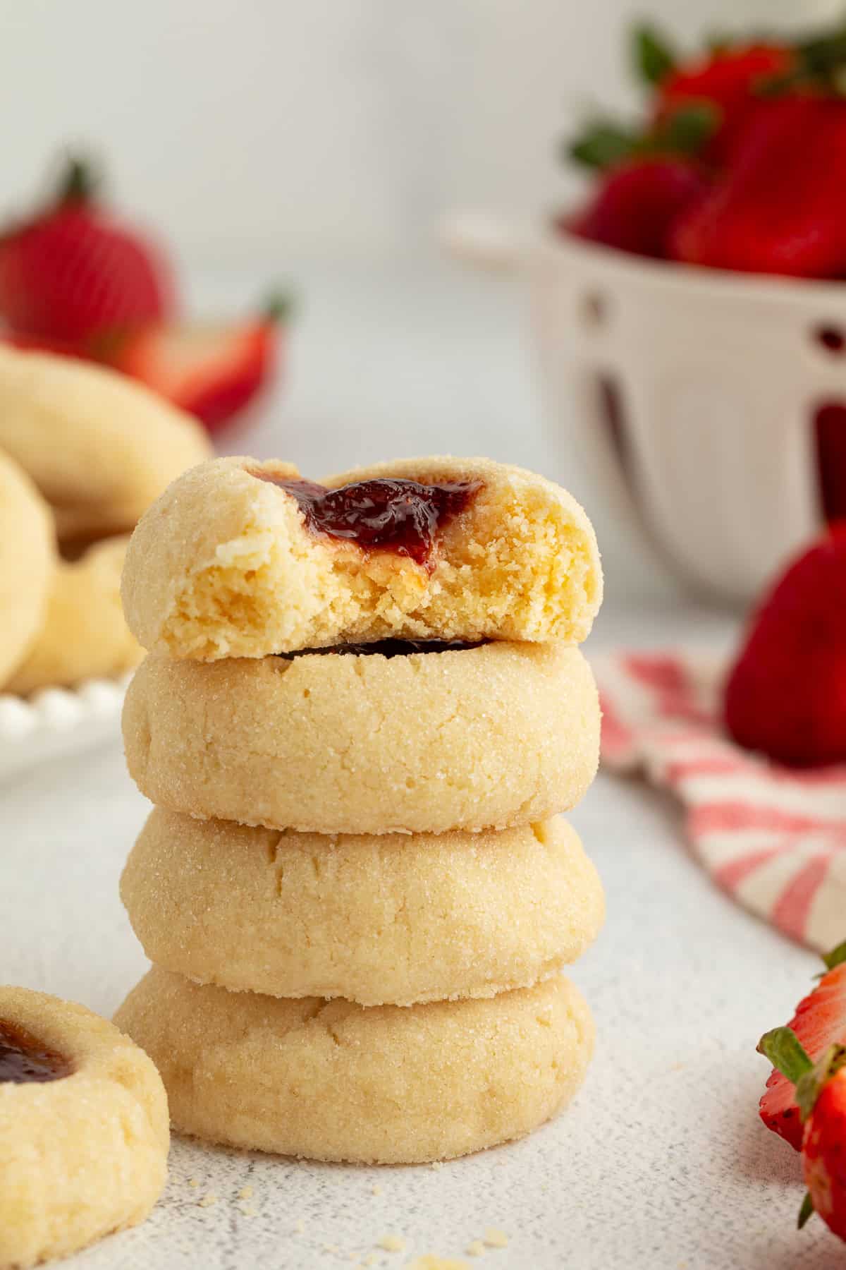 Thumbprint cookies are buttery, melt-in-your-mouth shortbread cookies rolled in sugar, filled with fruit jam, chocolate, caramel, and more. Four thumbprint cookies stacked with a bite missing from the top cookie.