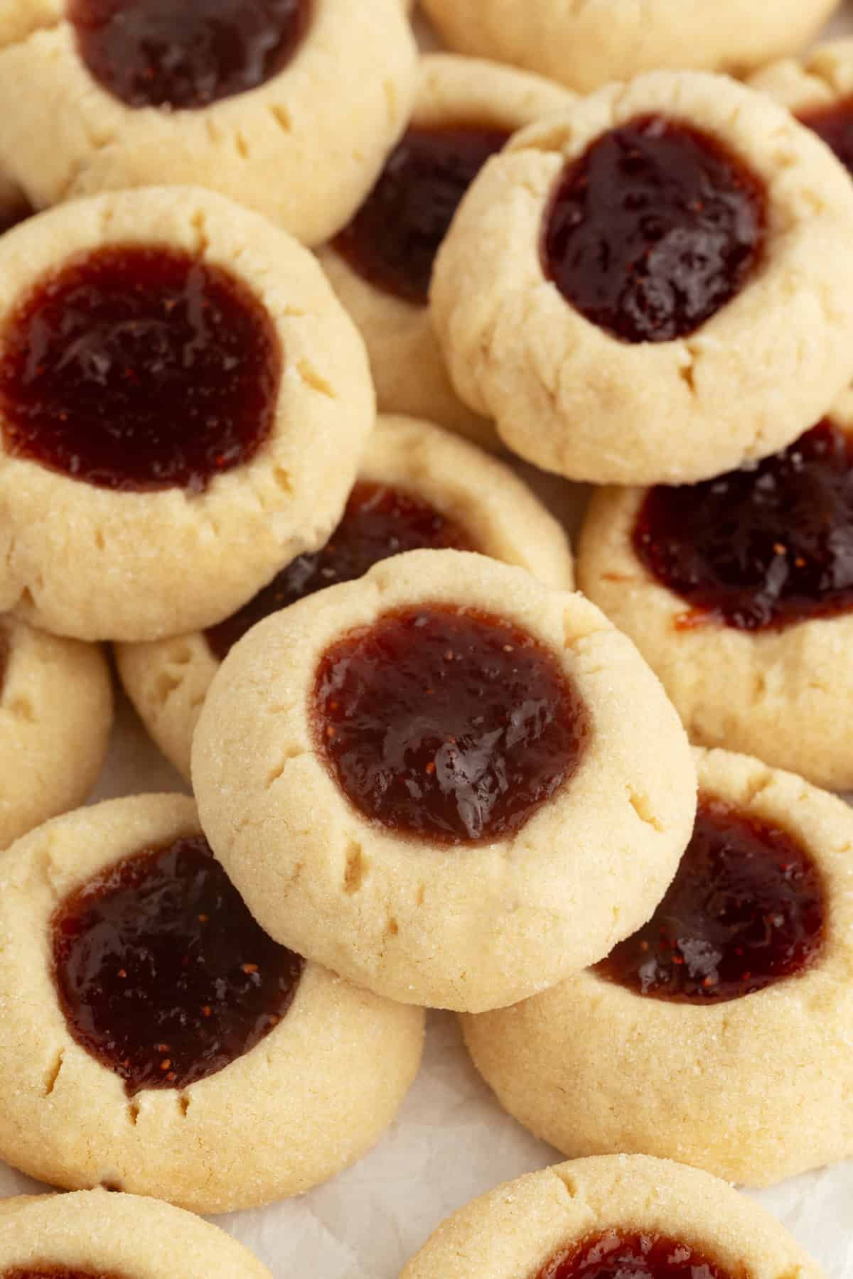 Thumbprint cookies are buttery, melt-in-your-mouth shortbread cookies rolled in sugar, filled with fruit jam, chocolate, caramel, and more. Overhead view of assorted jam-filled thumbprint cookies piled on a countertop.