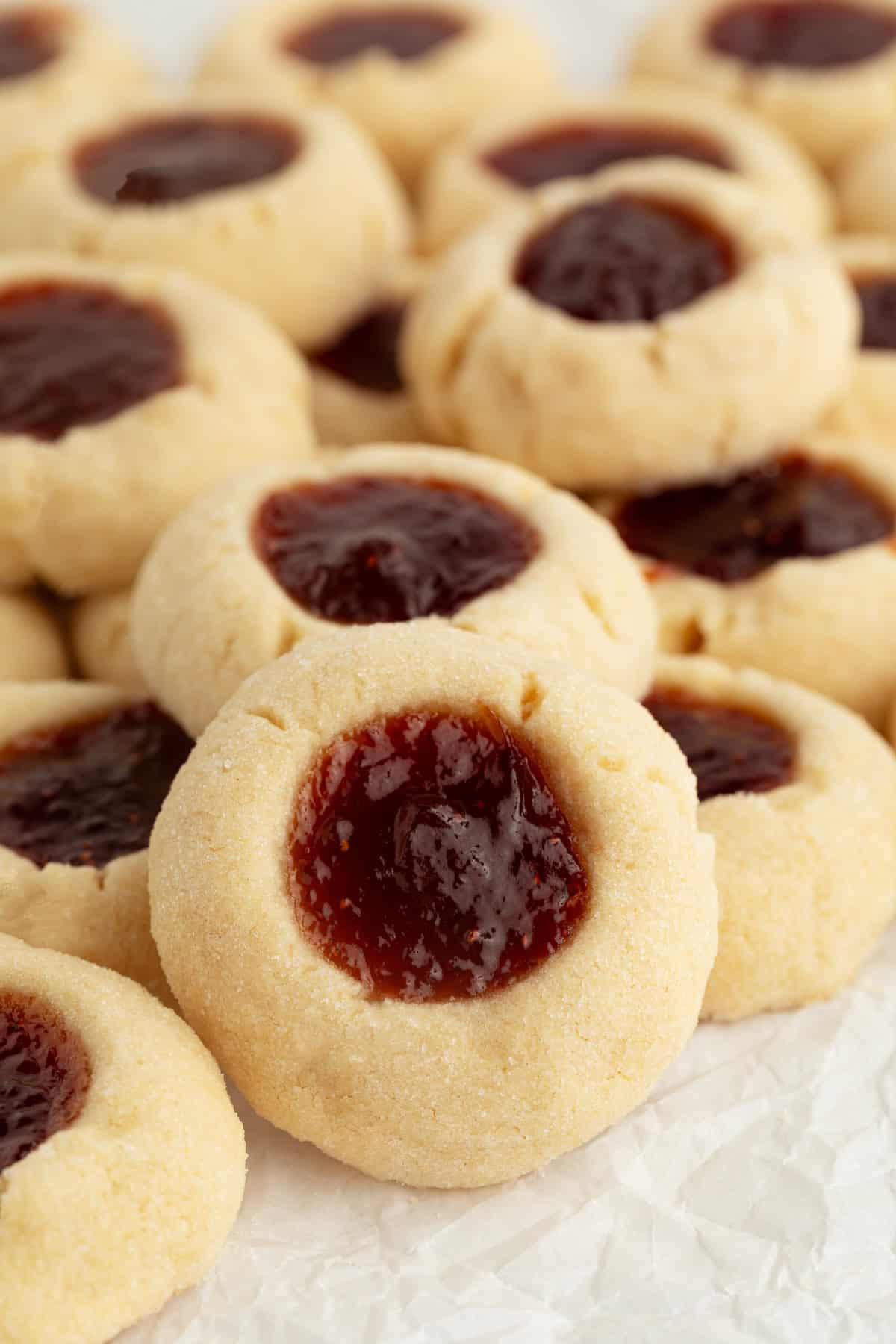 Thumbprint cookies are buttery, melt-in-your-mouth shortbread cookies rolled in sugar, filled with fruit jam, chocolate, caramel, and more. Assorted jam-filled thumbprint cookies piled on a countertop.
