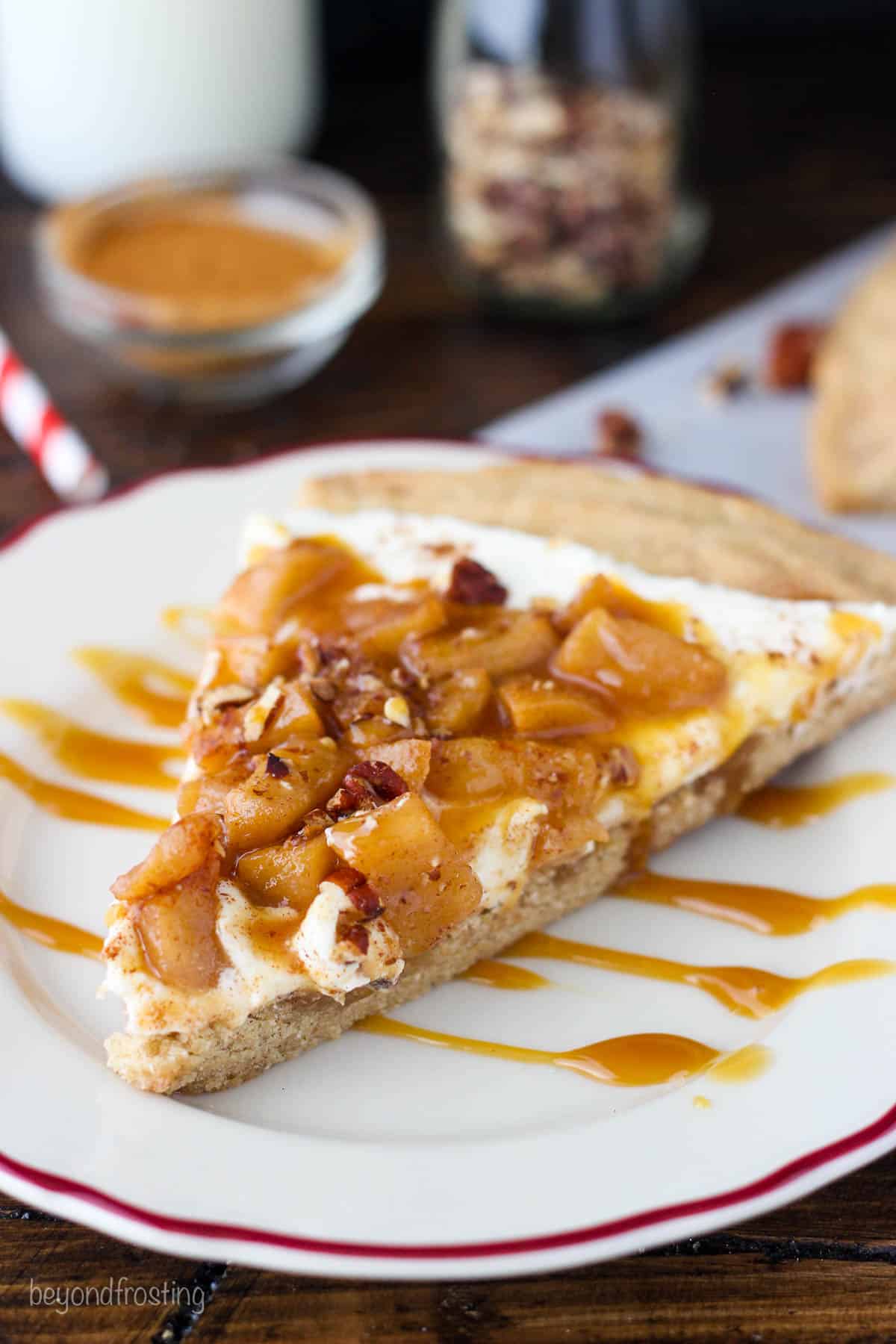 A piece of apple pie dessert pizza on a plate with a drizzle of caramel sauce on top of it