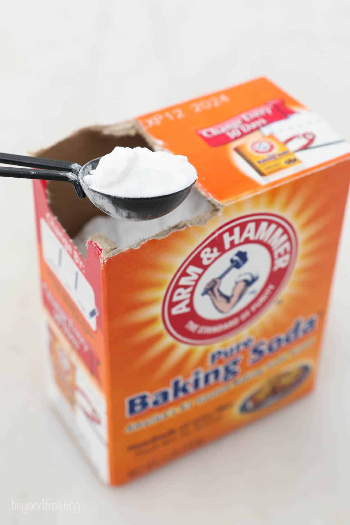 Baking soda being scooped out of a box by a black measuring spoon